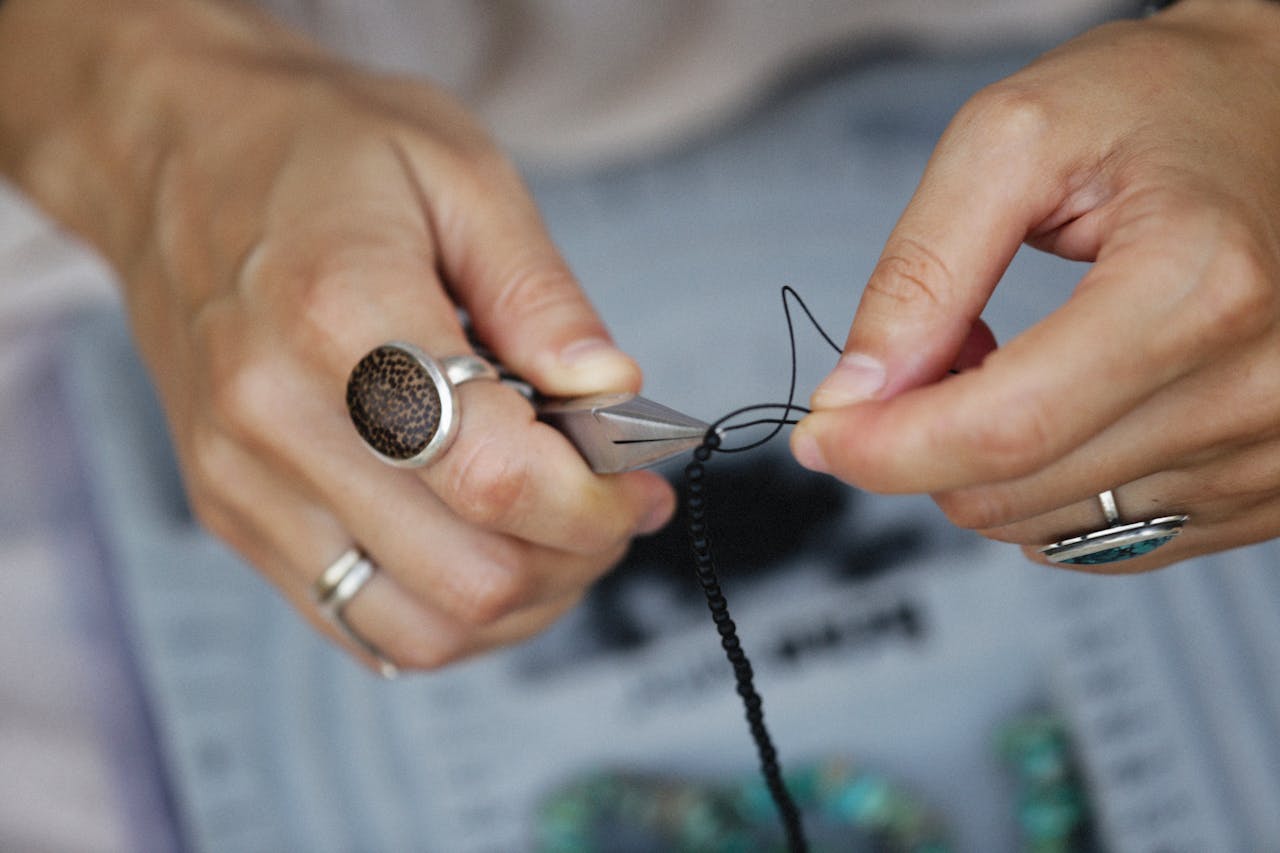 Detailed view of hands crafting handmade jewelry with beads and tools.
